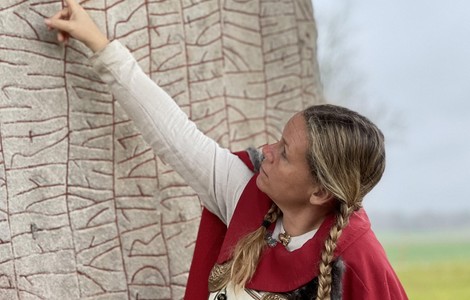 En vikingakvinna som pekar mot runstenen Rökstenen.