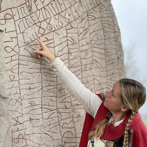 En bild på en vikingakvinna som pekar på en runstens-skrift. 