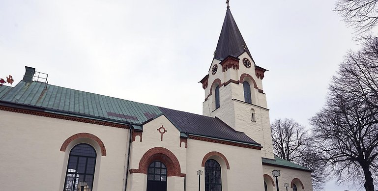 Ett foto över Ödeshögs kyrka. På bilder ser man en stenkyrka med beige puts, mörkt plåttak och ovala valvfönster. Till höger sitter klocktornet med samma detaljer. 